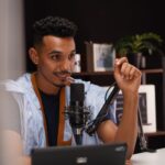 Confident young man speaking into a microphone during a podcast recording in a modern studio.