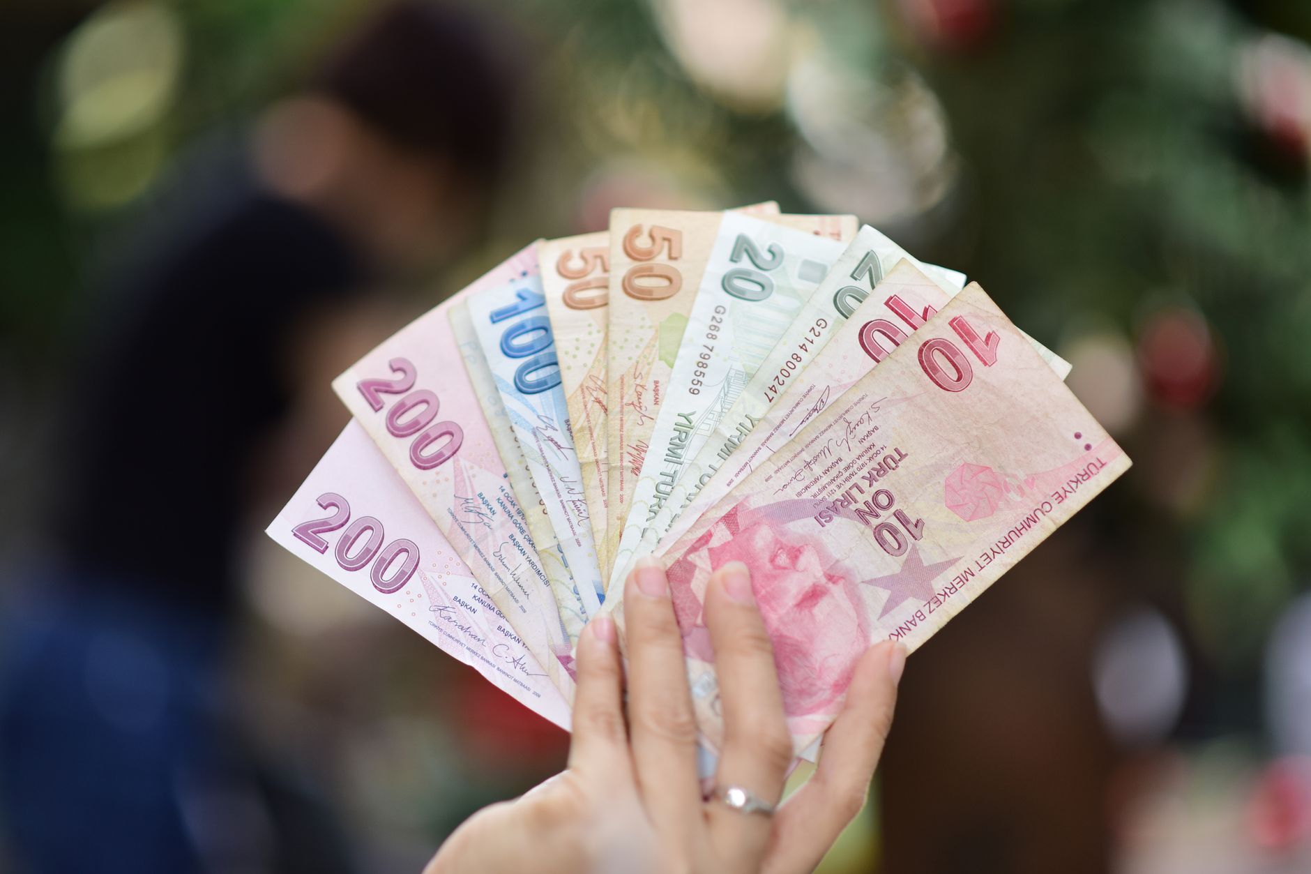 Close-up of a hand displaying various Turkish Lira banknotes outdoors.