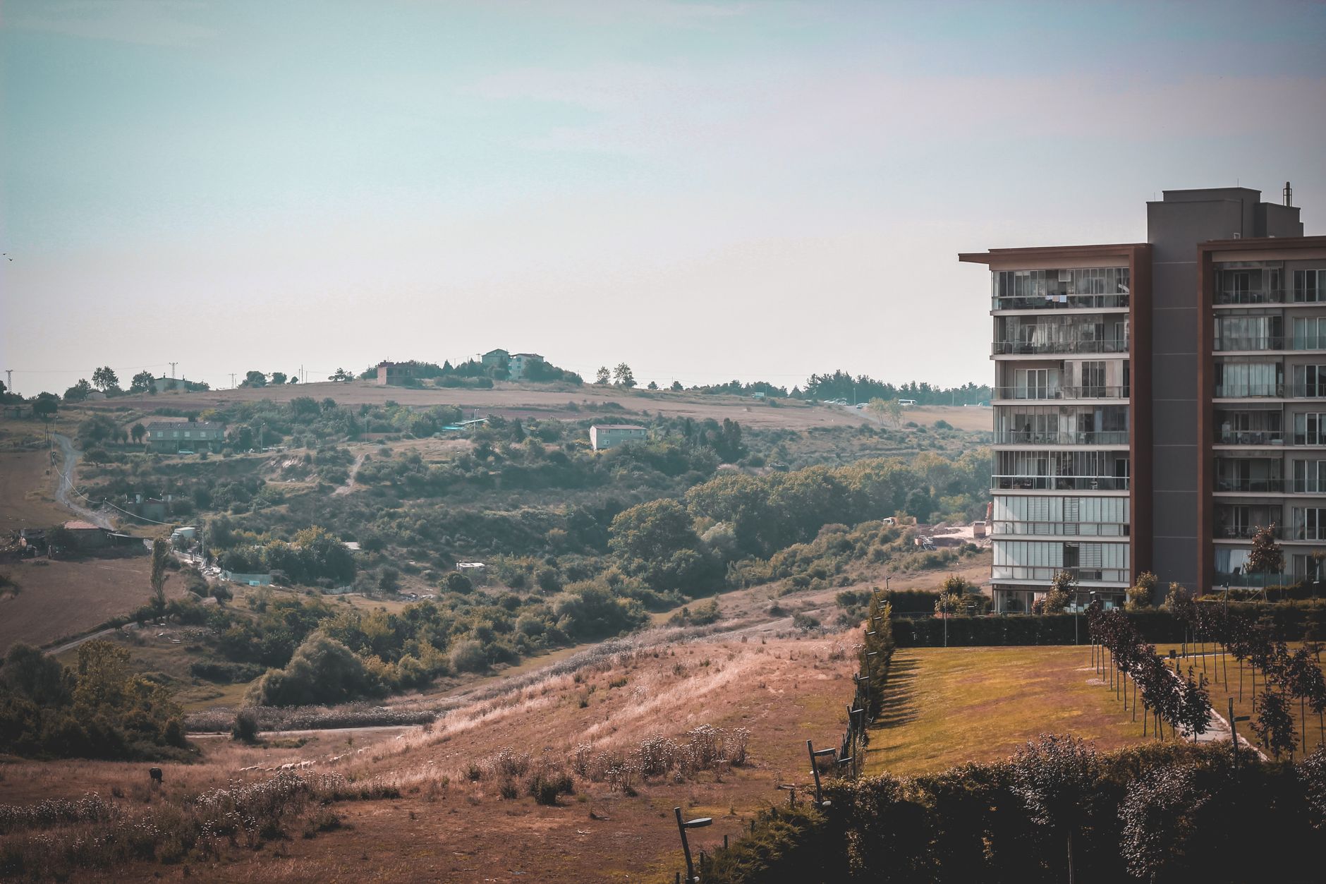 A modern high-rise residential building against the backdrop of Istanbul's scenic countryside and rolling hills.